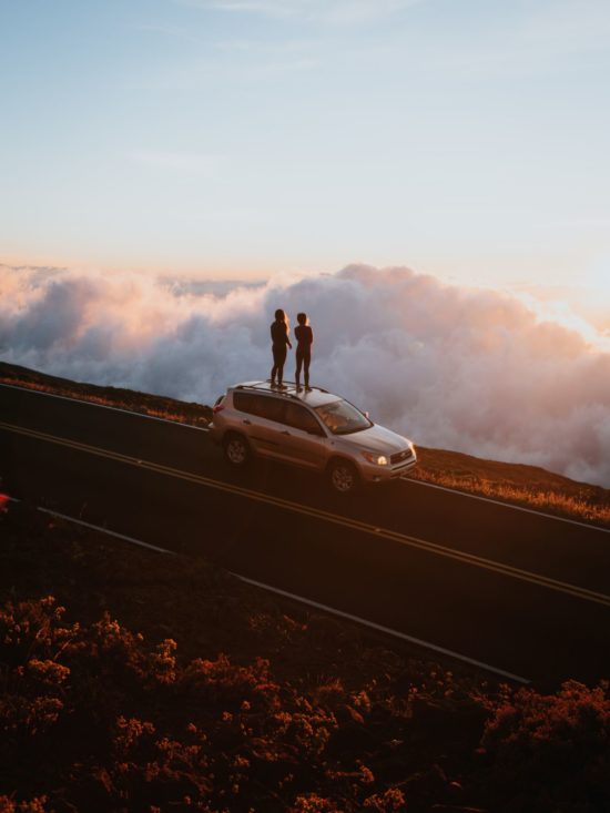 Nikki and Cole standing on their vehicle watching the sunrise at Mt. Haleakala in Maui, HI.